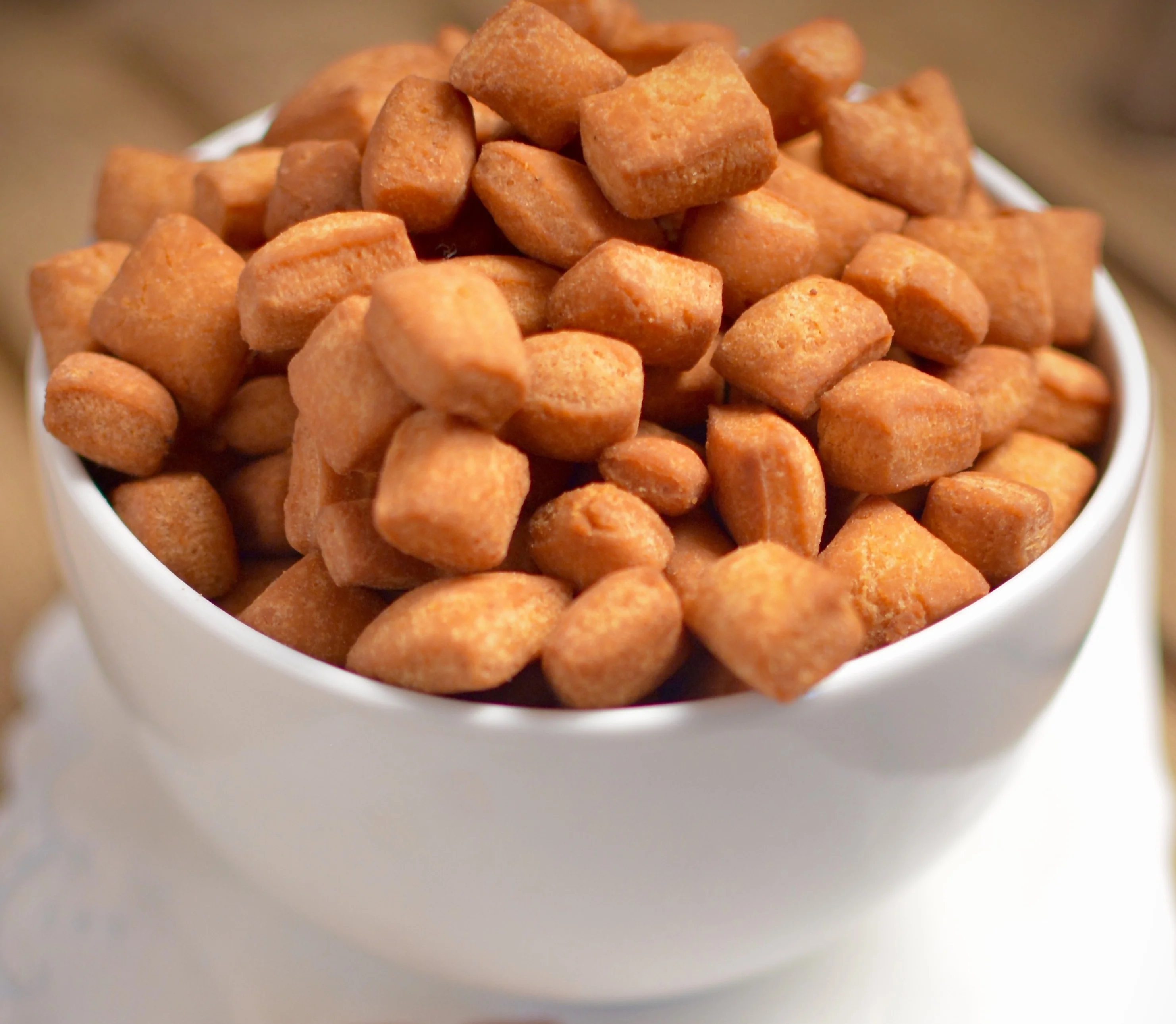 A white bowl filled with golden brown chinchin pieces stacked high, sitting on a light surface in a warm and inviting kitchen setting